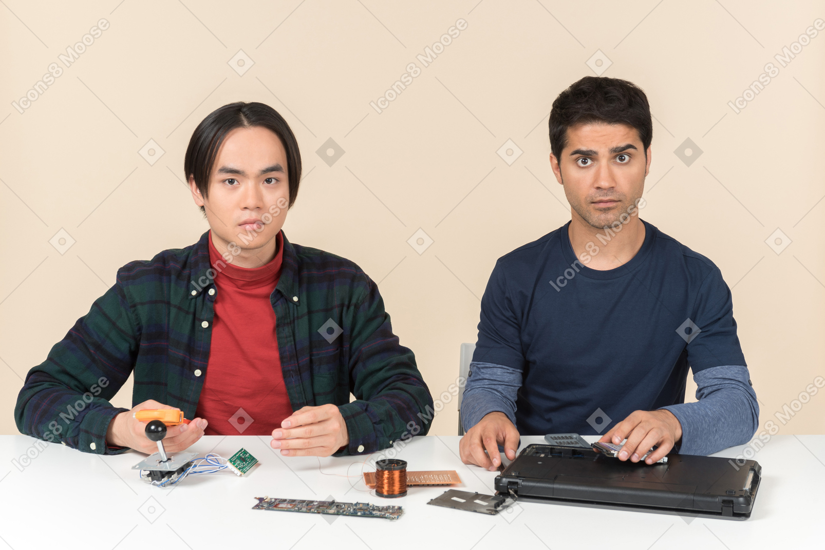 Two young geeks sitting at the table and fixing laptop