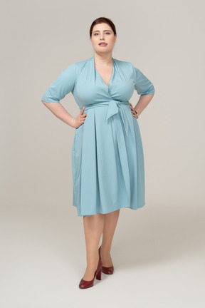 Front view of a woman in blue dress posing with hands on hips and showing tongue