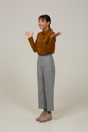 Vista de tres cuartos de una joven asiática encantada en calzones y blusa levantando las manos