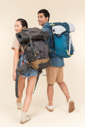 Joven mujer y hombre con enormes mochilas cogidos de la mano y mirando hacia atrás