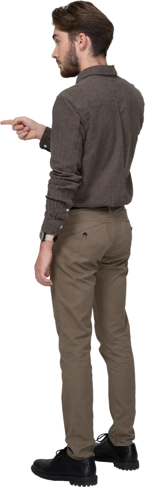 Трехчетвертный вид сзади молодого человека в офисной одежде, указывающего пальцем вперед
