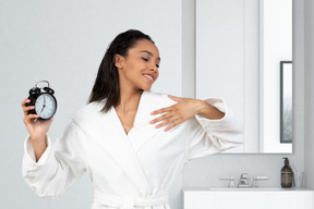 A woman in a bathrobe holding an alarm clock