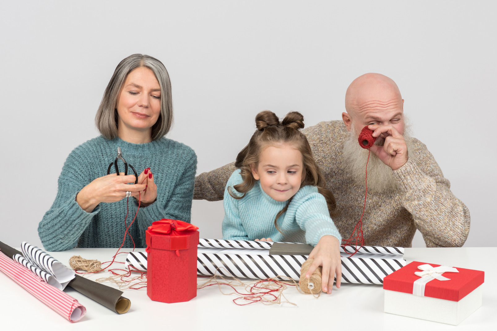Grandparents and kid girl sitting at the table and wrapping christmas gifts