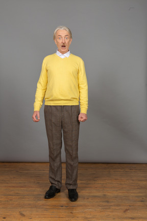 Vista frontale di un uomo scioccato in un pullover giallo in piedi ancora con la bocca aperta