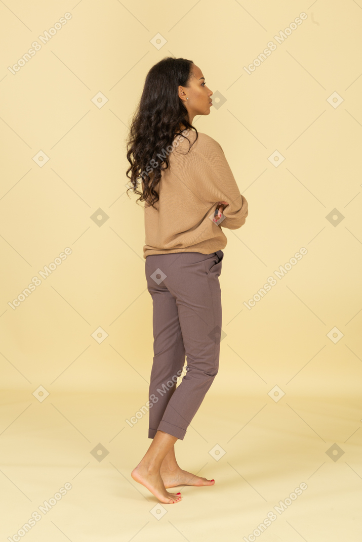 Vista de três quartos das costas de uma jovem mulher de pele escura cruzando os braços