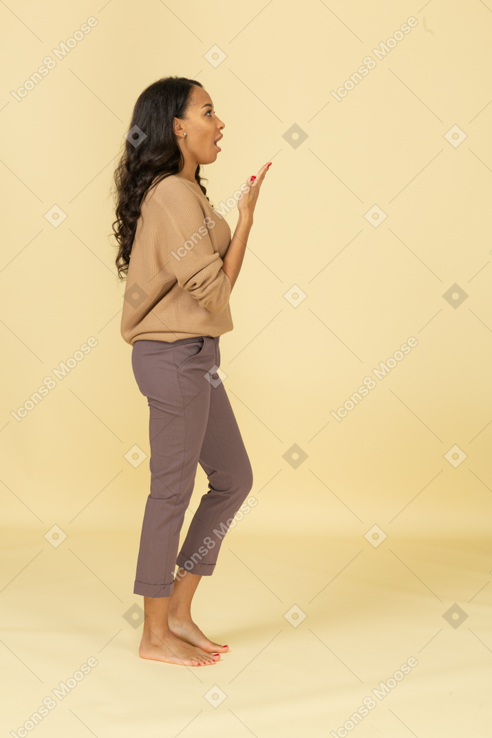 Vista lateral de uma jovem mulher de pele escura falando e levantando a mão