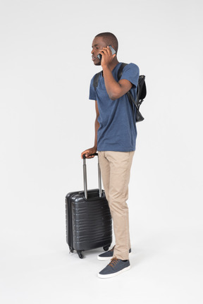 Male black tourist carrying luggage and talking on the phone
