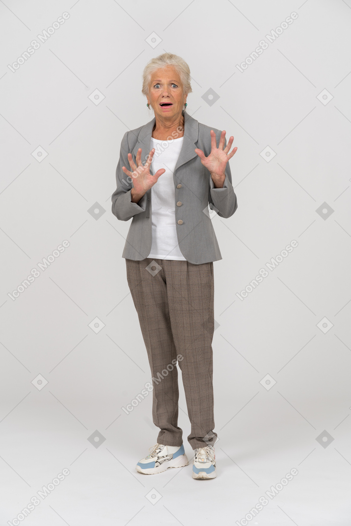 Vista frontal de una anciana asustada en traje mirando a la cámara y gesticulando