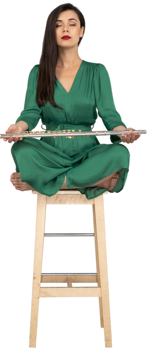 Девушка в полный рост, держащая кларнет на коленях, сидя на деревянном стуле