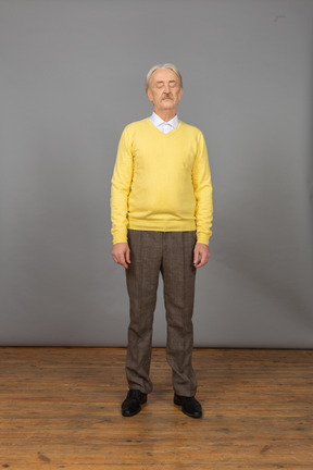 Vista frontal de um velho vestindo um pulôver amarelo e parado com os olhos fechados