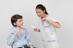 Female dentist showing to kid boy patient's how to brush teeth