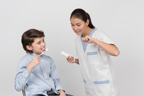 Dentista femenina mostrando a niño chico paciente cómo cepillarse los dientes