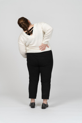 Retrovisor de uma mulher gorducha de suéter branco, sofrendo de dores na região lombar