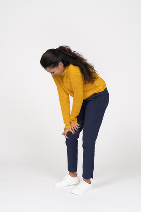 Side view of a girl in casual clothes bending down and touching her hurting knee