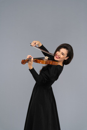 Close-up de uma jovem alegre de vestido preto tocando violino