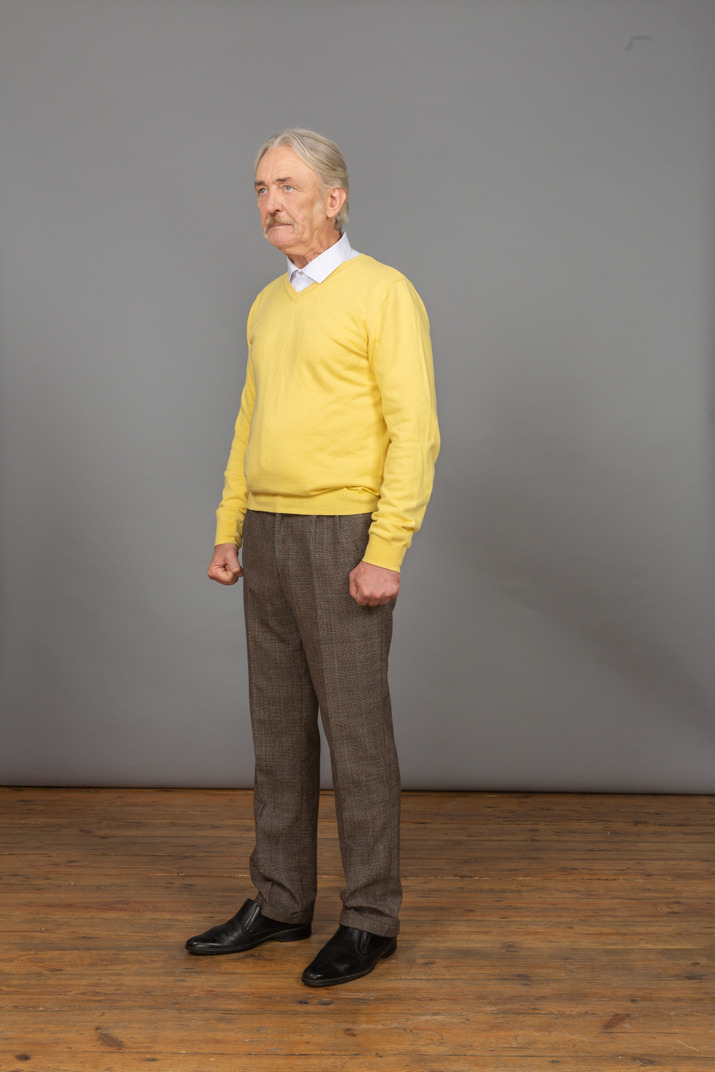 Three-quarter view of an old mad man in yellow pullover clenching fists