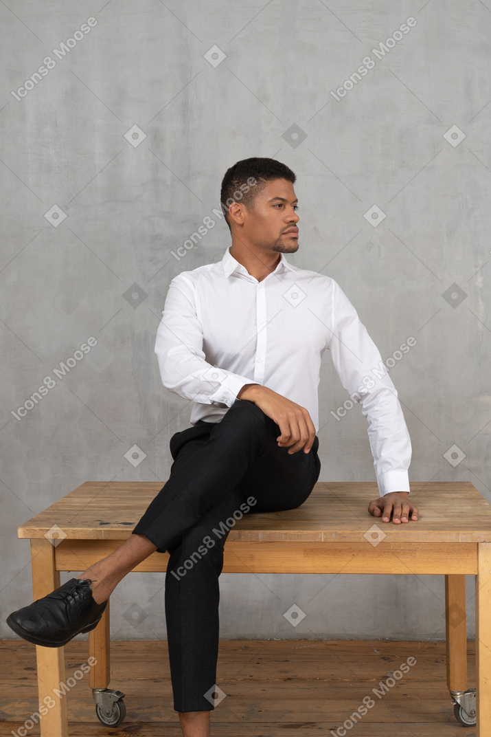 Gut gekleideter mann, der mit gedrehtem kopf auf einem tisch sitzt