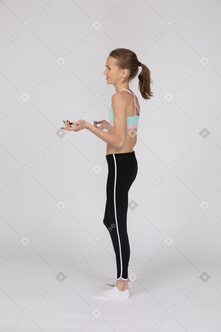 Вид сбоку недовольной девушки-подростка в спортивной одежде, поднимающей руки