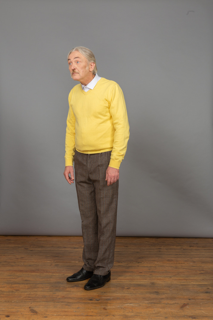 Three-quarter view of an old surprised man in yellow pullover leaning forward and looking aside
