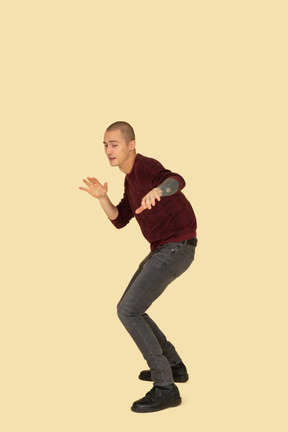 Side view of a cautious young man dressed in red pullover outstretching his hands