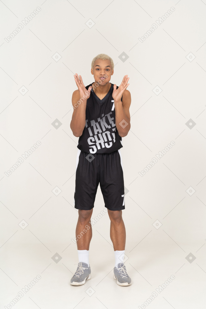 頬を吹いて手を上げる若い男性バスケットボール選手の正面図
