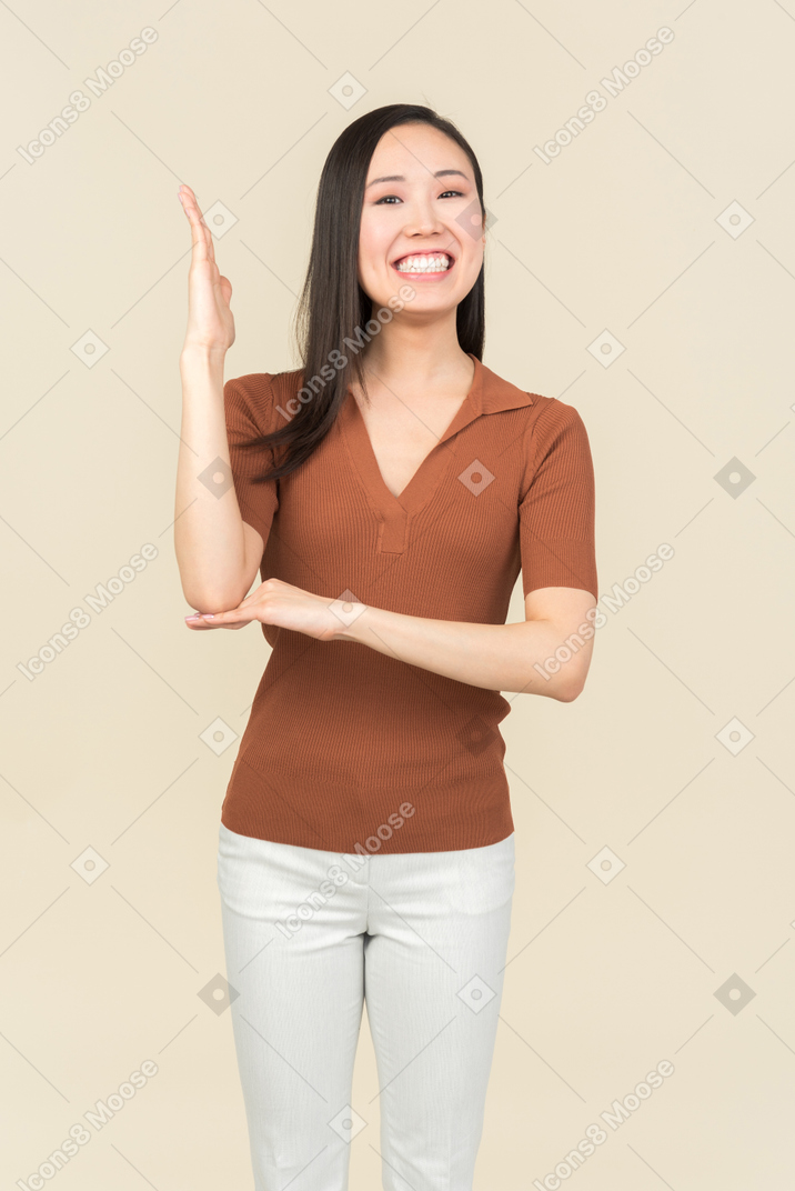 Smiling young asian woman holding one hand up