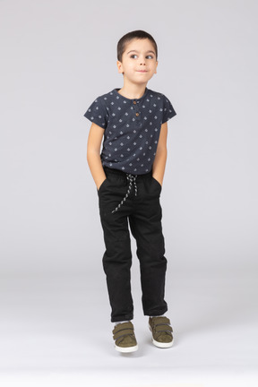 Vue de face d'un garçon mignon dans des vêtements décontractés posant avec les mains dans les poches et regardant la caméra
