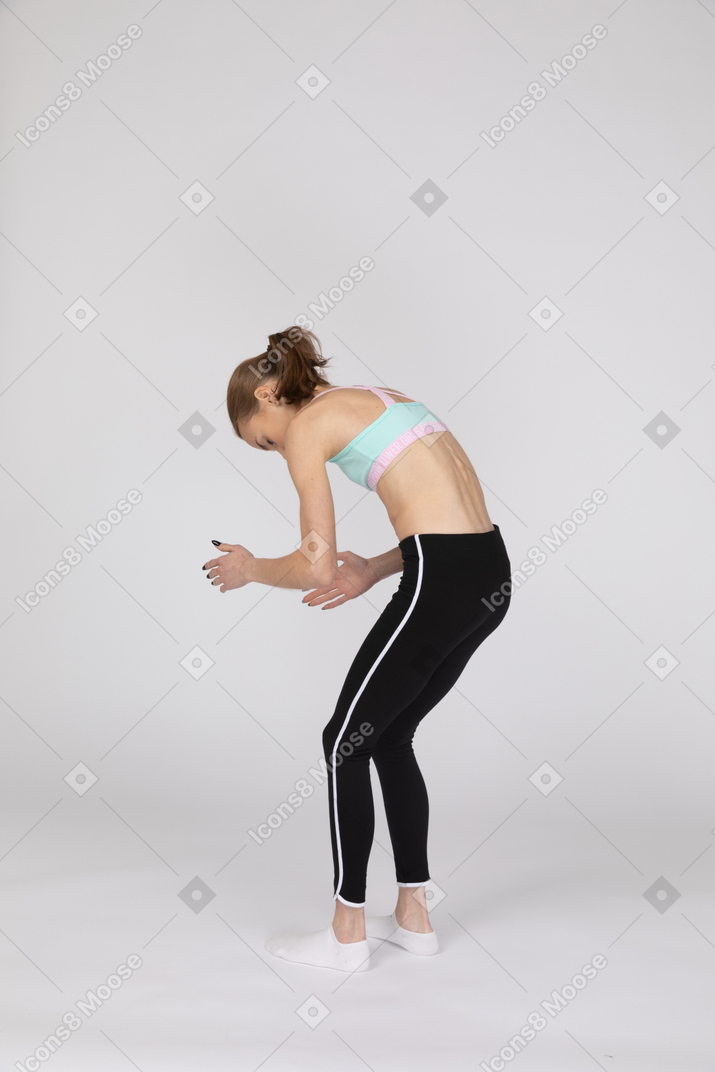 Three-quarter back view of a teen girl in sportswear bending over and raising her hands