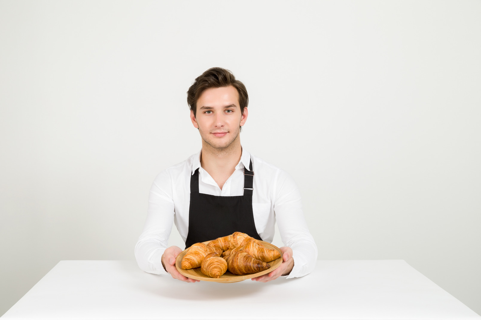 Male chef sitting at table with plate of croissants