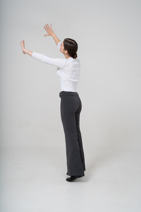 腕を上げて立っている黒いズボンと白いブラウスの女性の側面図