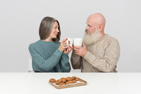 Pareja de ancianos diciendo saludos con tazas de café