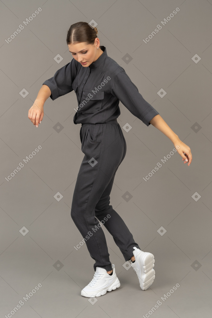 Вид сбоку танцующей молодой женщины в комбинезоне, смотрящей вниз