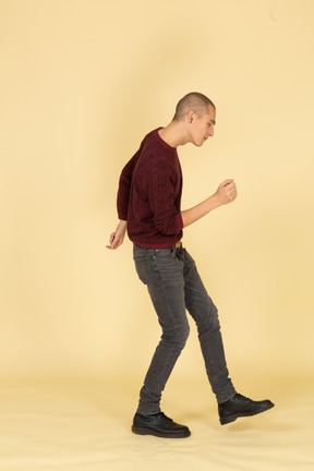Вид сбоку танцующего молодого человека в красном пуловере, поднимающего ногу