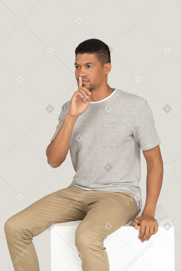 A good looking beautiful man sitting on the white chair and making silence gesture