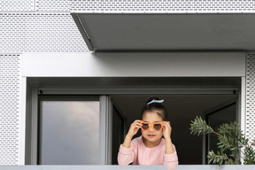 A little girl wearing sunglasses looking out of a window