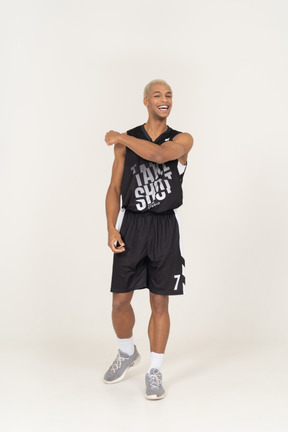 Vista frontale di un giovane giocatore di basket maschio sorridente che tocca la spalla