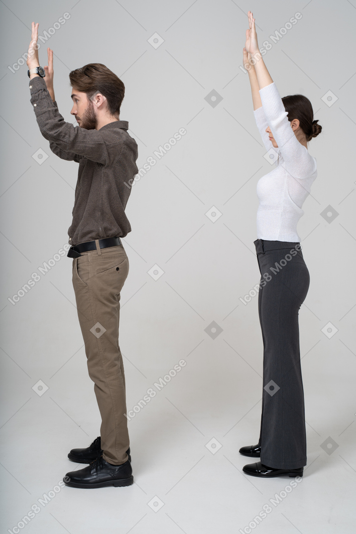 Side view of a young couple in office clothing raising hands