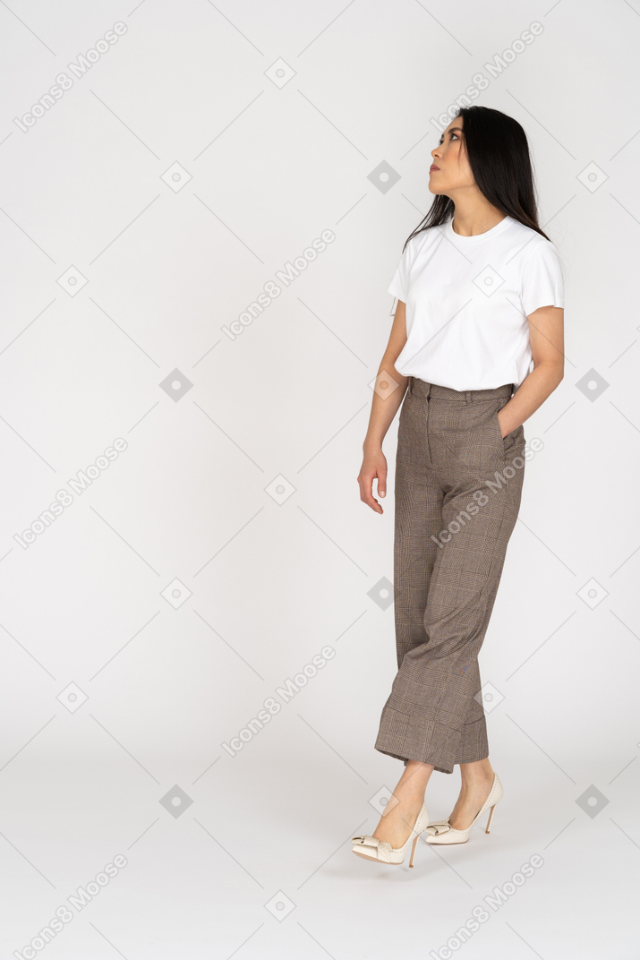 Vista di tre quarti di una giovane donna che cammina in calzoni e t-shirt alzando lo sguardo