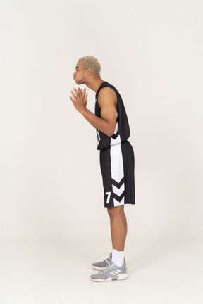 Vista lateral de um jovem jogador de basquete soprando bochechas e levantando as mãos