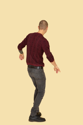 Three-quarter back view of a dancing young man dressed in red pullover