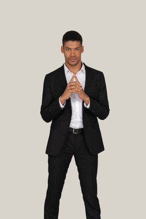 Pensive young man in black suit standing with his hands folded