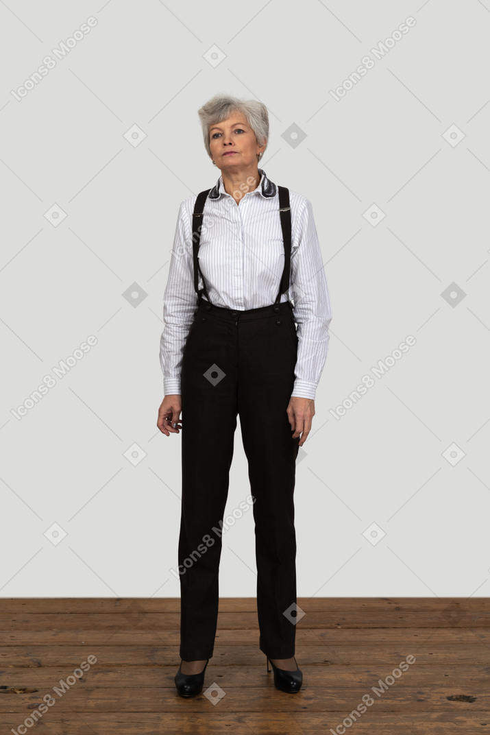 Vista frontal de uma mulher velha descontente com roupas de escritório, parada na sala