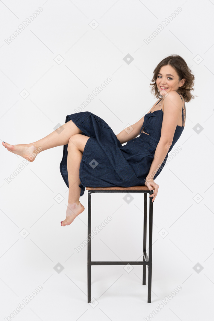 Веселая девушка сидит нога к ноге на барном стуле