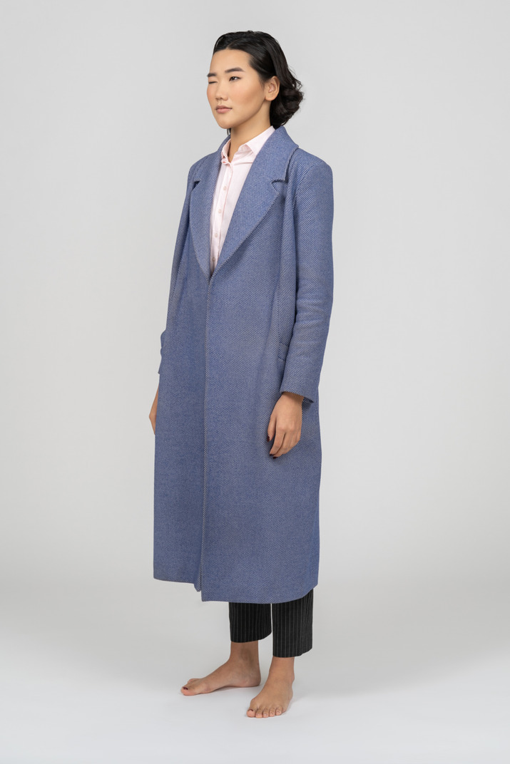 Young asian woman in long blue coat standing half sideways