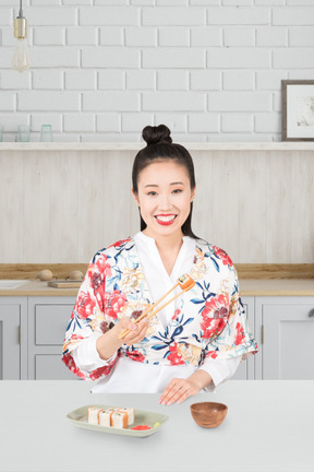 A woman in a kimono holding chopsticks and a bowl of sushi