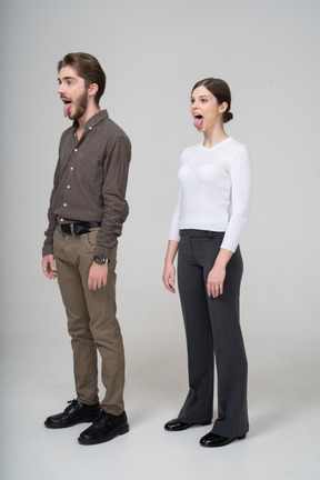 Vista di tre quarti di una giovane coppia pazza in abiti da ufficio che mostra la lingua