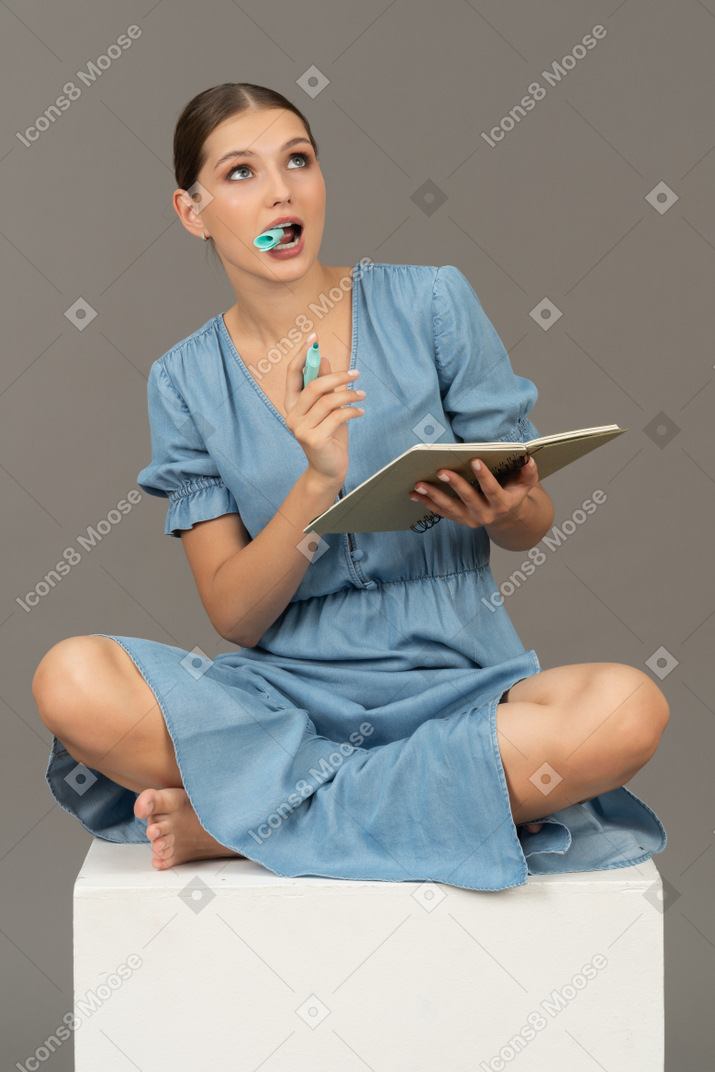 坐在立方体上的年轻女子的正面图，上面有记号笔和笔记本