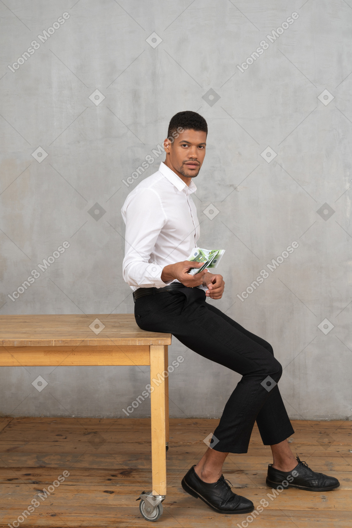 Man in formal clothes sitting on a table and holding money