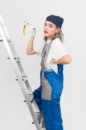 Female worker standing on stepladder and holding pliers