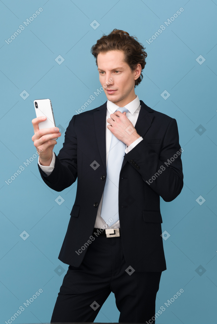 Adjusting his tie while looking at smartphone display
